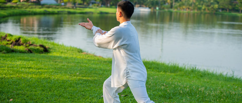 Young man practicing traditional Tai Chi Chuan, Tai Ji and Qi gong in the park for healthy, traditional Chinese martial arts concept.