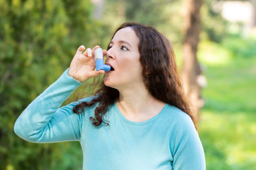 Woman is using an asthma inhaler in a park