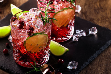 Refreshing drink with cranberries, ice and rosemary on wooden background, red cocktail, copy space