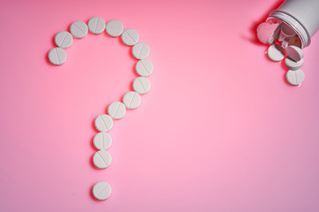 The Question mark of the pills.Question point. White pills on a pink background. Important information on medical topics. Copy space.
