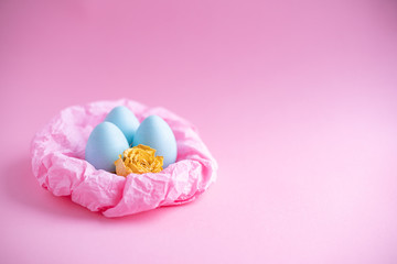 Easter eggs are blue in a paper nest and a yellow rose is a dried flower on a pink background. Top view free space for copying. Easter concepts