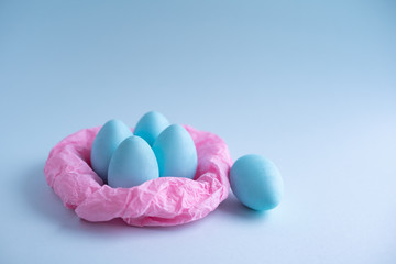Blue Easter eggs in a pink paper nest on a blue background. Top view free space for copying. Easter concepts