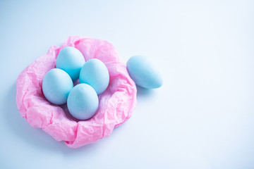 Blue Easter eggs in a pink paper nest on a blue background. Top view free space for copying. Easter concepts