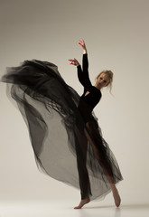 Woman dancer in a long black dress waves her arms up. The fabric of a long tulle skirt flies...