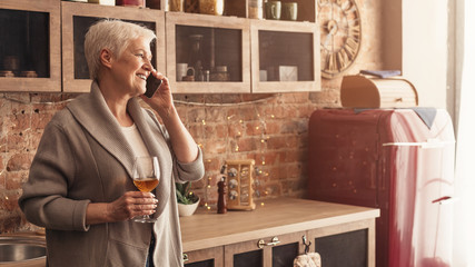 Happy senior woman enjoying glass of wine while talking on cellphone