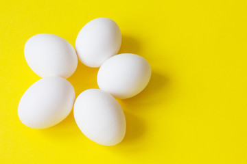 Five white eggs lie on a bright yellow background in the shape of a flower.