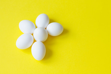 Six white eggs lie on a bright yellow background in the shape of a Daisy.