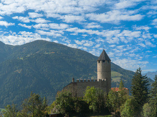 Fototapeta premium High tower of the fortress with a protective wall and two peaks in the mountains of Alto Adige