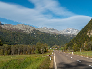Fototapeta na wymiar Direct rural asphalt road in the Alpine mountains valley in autumn, blue sky background