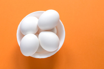 A few white eggs in a bowl on a colorful terracotta background.