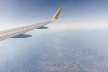 ala de un avión airbus a320 sobrevolando montañas españolas, de fondo el cielo con nubes en un dia azul, soleado y claro. avión de transporte humano.