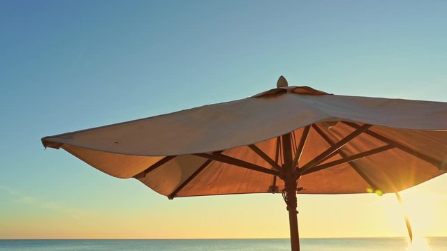Brown sun umbrella against clear sky on sunset, sea water on horizon, close up