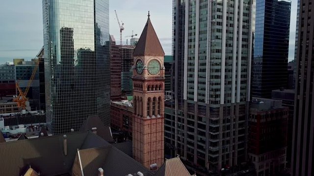 Historic Clock Tower surrounded by Tall Modern Glass Office Skyscrapers, Aerial Parallax Orbit Pan. Wide Drone shot of Old City Hall at Nathan Phillips Square in Toronto Ontario Canada near Sunset