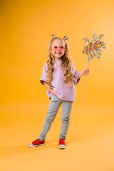 happy cute little girl with long blonde hair holding a baby windmill on a yellow background