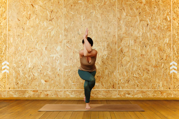 Eagle pose (Garudasana), woman practicing yoga poses on wooden background.