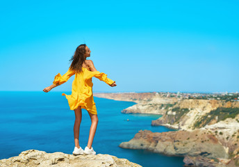 Full length portrait of taned traveler woman standing on top rock beach with open arms, bright...