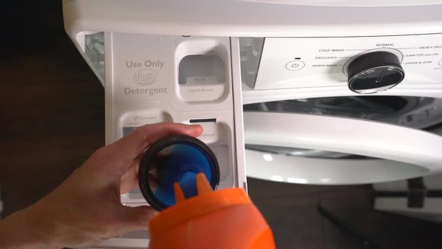 Person measuring and pouring HE laundry detergent into front loading washing machine. Top down view