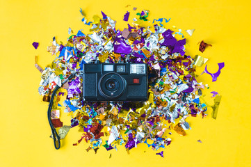 Old photo camera placed on colored streamers and a yellow background