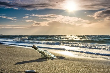 message in a bottle on the beach - old glass bottle with a message on the beach with dramatic...