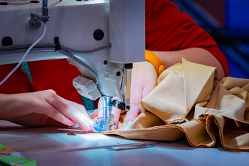 Woman sews clothes. Work as a seamstress. Female hands next to a working sewing machine. Girl works in a garment factory. Work on an industrial sewing machine. Manufacture of wearing apparel