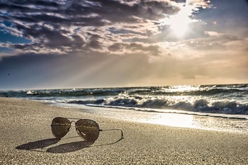 sunglasses on the beach with colored sunset with cloud cover over the sunset at the beach - dramatic sunset on the baltic sea
