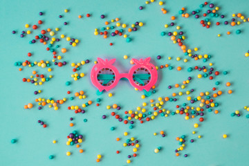 Pink sunglasses with colored balls around on an aquamarine blue background
