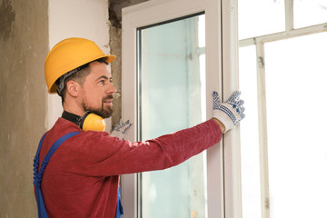 Worker in uniform installing plastic window indoors