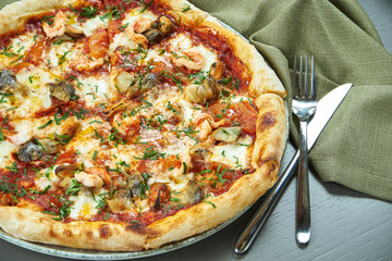 Close up view on appetizing pizza with red sauce, mussels and shrimp on wooden background in a restaurant. Italian cuisine. Selective focus