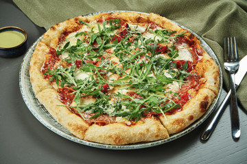 Close up appetizing pizza with prosciutto, arugula, tomatoes, parmesan and mozzarella on wooden background in a restaurant. Italian cuisine. Pizza on center composition