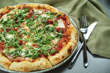 Close up appetizing pizza with prosciutto, arugula, tomatoes, parmesan and mozzarella on wooden background in a restaurant. Selective focus, copy space