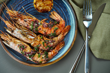 Grilled tiger prawns with lemon in a blue plate on a wooden background. Luxury seafood top view with copy space. Flat lay