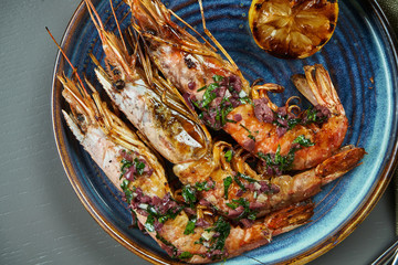 Grilled tiger prawns with lemon in a blue plate on a wooden background. Luxury seafood top view. Flat lay. Close up