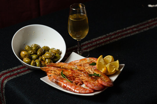Gambones, copa de vino y olivas verdes encima de una mesa 