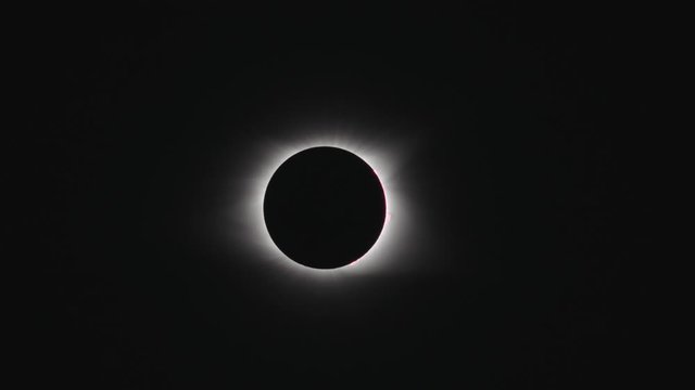 A telephoto shot of the total solar eclipse as it ends in a beautiful flare. Clouds sweep across the scene.