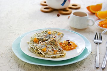 Thin crepe pancakes with poppy seeds, orange jam and chopped hazelnuts on a white plate on a light concrete background. French cuisine Pancake day concept. Pancake Recipes. Copyspace.