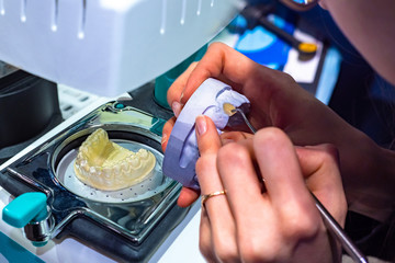 Hands of a dental technician with a mock-up of the jaw and a dental instrument in close-up. The production of accurate copies of the jaws for a correct treatment. Denture. Manufacturing of prostheses.