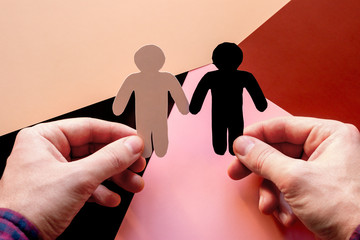 man holds black and white cardboard silhouettes on a colored background. stop discrimination and...