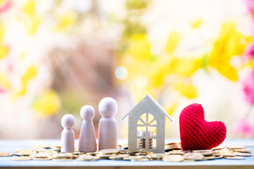 Home and stack gold coin with growing value money and light bulb and red heart and family put on the wood in the public park, Idea of investing in buying a real estate or decorating a house concept.