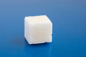 One piece of white sugar on a blue background, close-up
