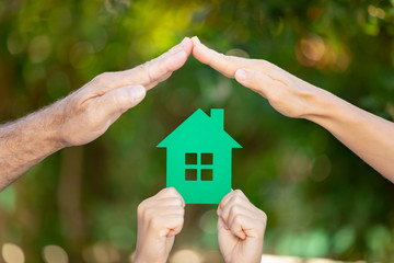 Family holding house in hands against spring green background