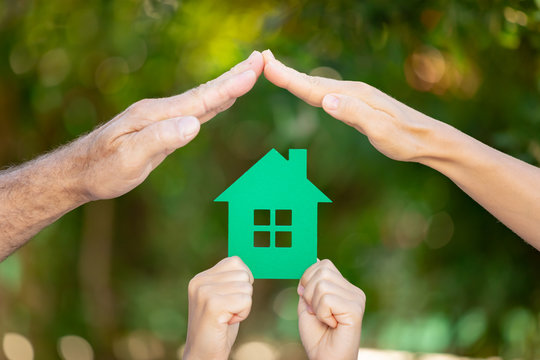 Family Holding House In Hands Against Spring Green Background