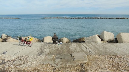 Pescatore con la canna da pesca e la bicicletta in riva al mare in una giornata d'autunno