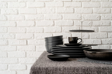 stack of black ceramic dishes and tableware on the table on white brick wall background