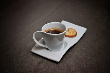 Una deliciosa taza de café caliente servido en porcelana blanca acompañado de galletas y granos de café