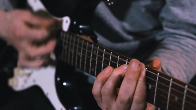 Guitarist hits the strings of the electric guitar, close up mens fingers playing music on guitar in slow motion