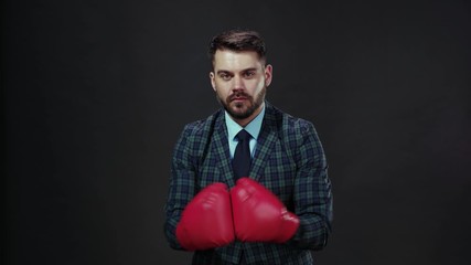 Confident brave business young man in suit wears boxing gloves and punches into air tempting to combat. Challenge, character, strong face. - Powered by Adobe