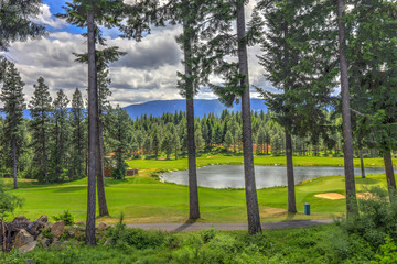 Golf course with pine trees and pond in cascade mountains of Northwest with little house.
