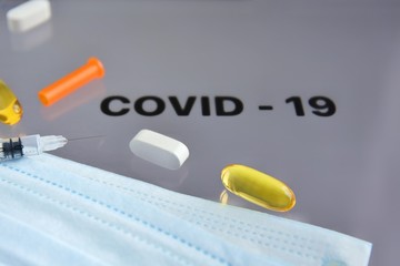 Inscription COVID-19 on display with pills, syringe, thermometer and protection mask on background. Dangerous asian ncov corona virus, dna, pandemic risk background design