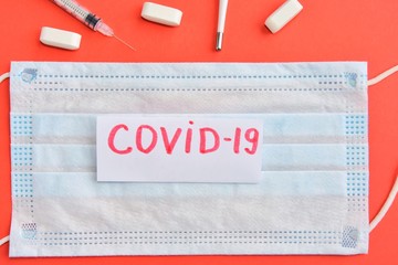 Protection sterile mask with an inscription covid-19 thermometer, syringe on orange background. Coronavirus disease named COVID-19. Healthcare concept. Virus vaccine