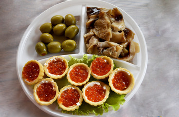 On the plate are several sectors in one tartlets with caviar, in the other olives and pickled mushrooms in the third. Plate with appetizer on the table.
